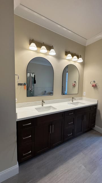 Remodeled bathroom with a double vanity, dark cabinetry and arched mirrors