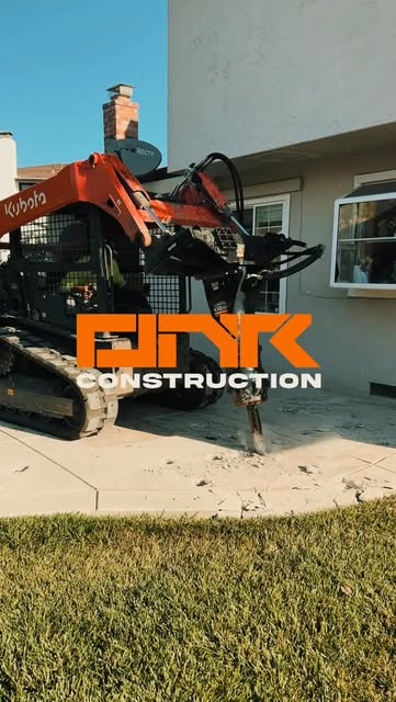 Track loader with a hydraulic breaker attachment removing old concrete beside a house
